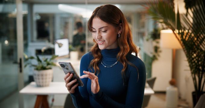 Business woman, cellphone and scroll in office at night for communication, contact or company email access. Female employee, technology and happy with feedback, social media target and deadline