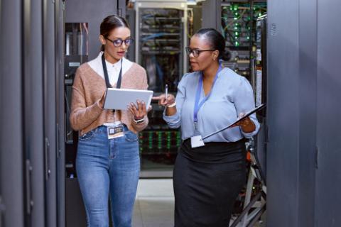 Talking, server room and women with a tablet for cyber security, database planning and inspection. Teamwork, technician and female programmers speaking with technology for coding, hardware and system