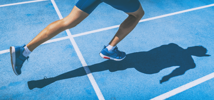 Sprinting man runner sprinter athlete running shoes and legs on track and field lane run race competing fast panoramic banner background.