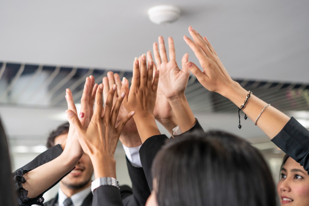 Many happy business people raise hands together with joy and success. Company employee celebrate after finishing successful work project. Corporate partnership and achievement concept.