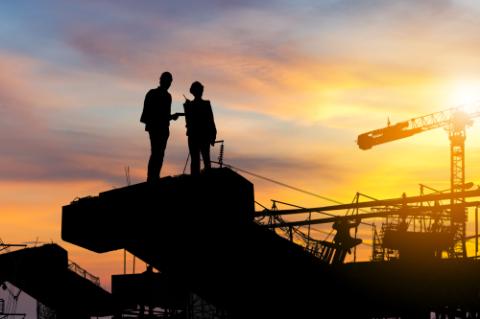 Silhouette of Engineer and worker checking project at building site background, construction site at sunset in evening time.