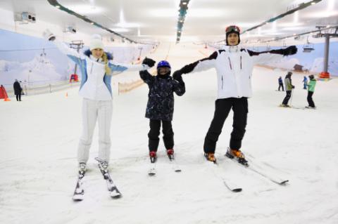 Husband, wife and child dressed in sports clothes standing on skis in indoor ski