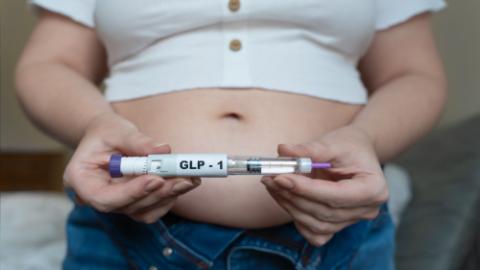 GLP-1 injection pen held by woman in front of abdomen, weight management concept