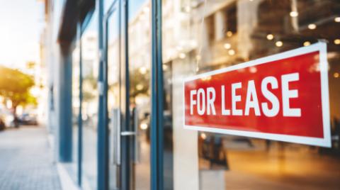 Storefront window displaying a red FOR LEASE sign, indicating available commercial property for business rental
