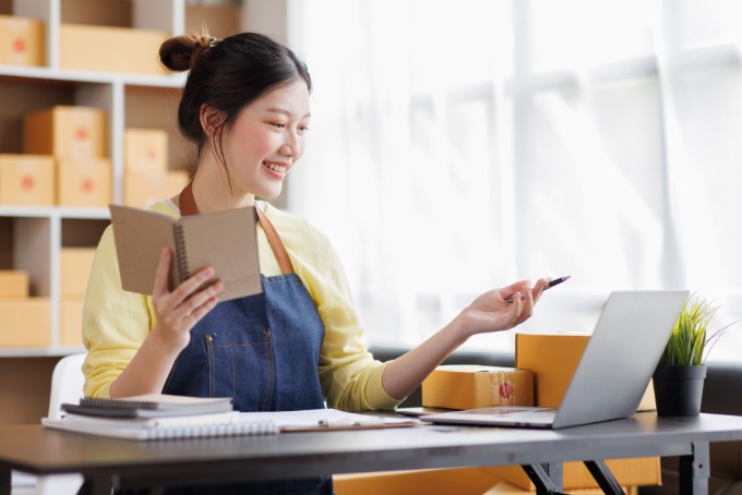 Startup SME small business entrepreneur of freelance Asian woman wearing apron using laptop and box to receive and review orders online to prepare to pack sell to customers, online sme business ideas.
