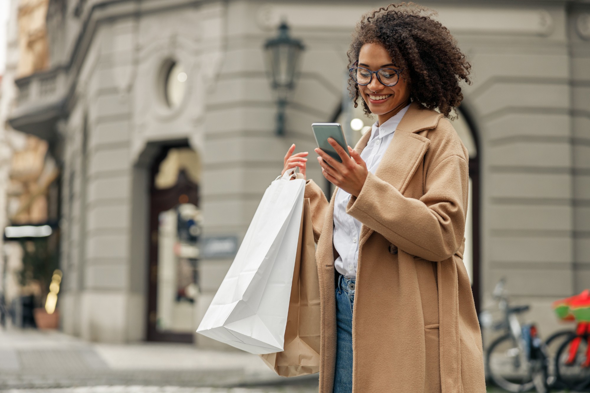 Fashion afro american woman after shopping with paper bags standing in city and using phone