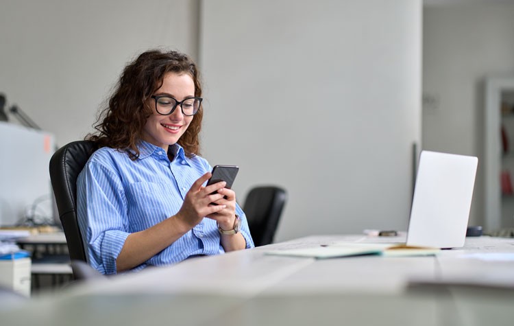 Young smiling business woman using phone working in office sitting at desk.