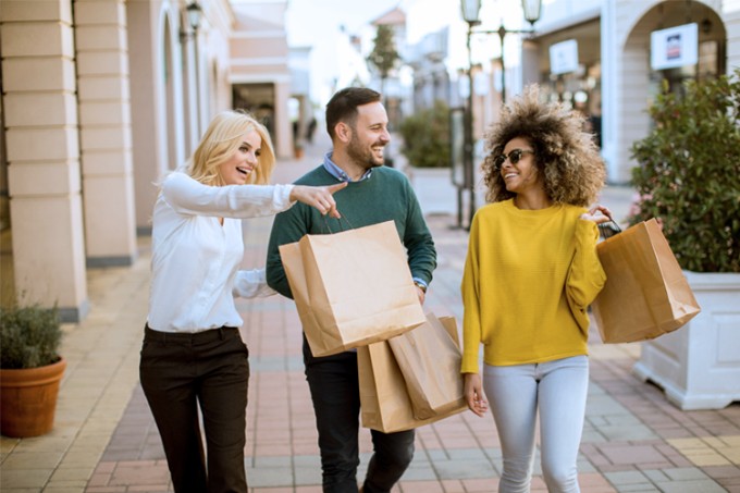 3 vrienden lopen over een shoppingstraat met zakken in de hand