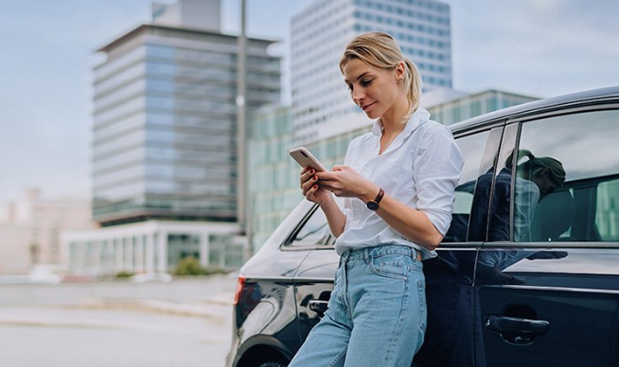 Vrouw staat met smartphone voor auto