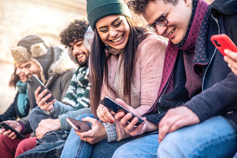 Teenagers group watching smart phones mobile outdoors - Diverse students sitting outside school using cellphones - Young people addicted to technology - Connection and youth concept