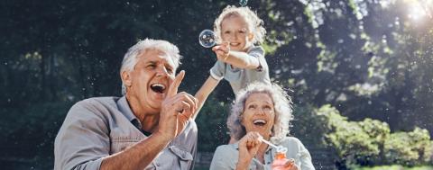 Grandparents, bubbles and children play in park happy together for fun, joy and outdoor happiness. Retired, smile and excited elderly senior couple, girl grandkids and love playing outside in nature