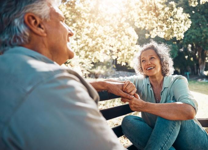 Elderly, couple and happy on bench in garden for conversation, bonding and happiness by trees in summer. Man, woman and retirement show love, relax and smile together in nature with sunshine at park