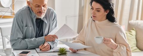 A man and woman sit at a table, surrounded by papers, engaged in a serious discussion.