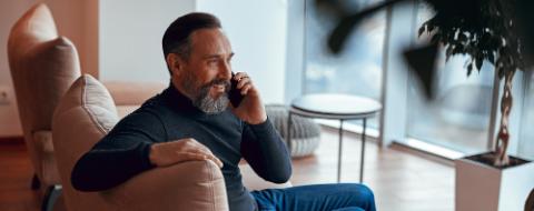 Happy bearded man sitting near window and chatting on phone